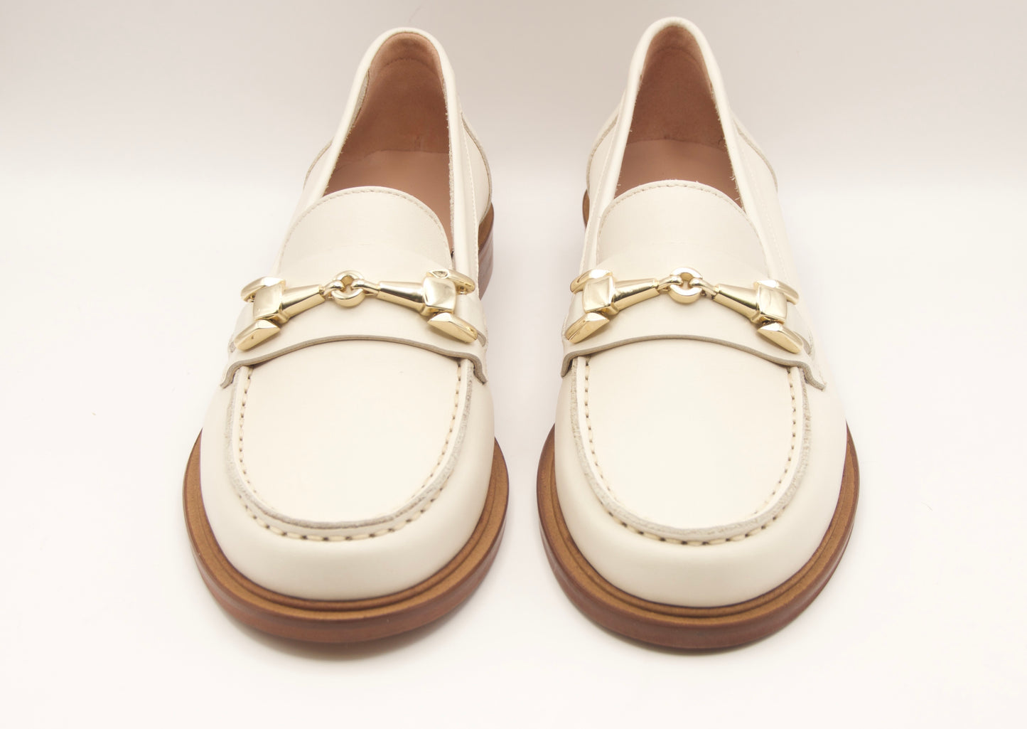 Pair of white loafers with gold accents on a light gray background